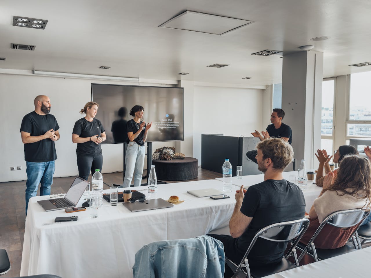 Team members presenting in a modern office with colleagues applauding.